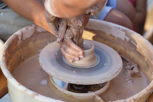 Hands of young potter, creating an earthen jar on the circle, close-up
