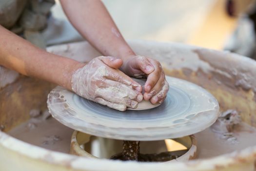 Hands of young potter, creating an earthen jar on the circle, close-up