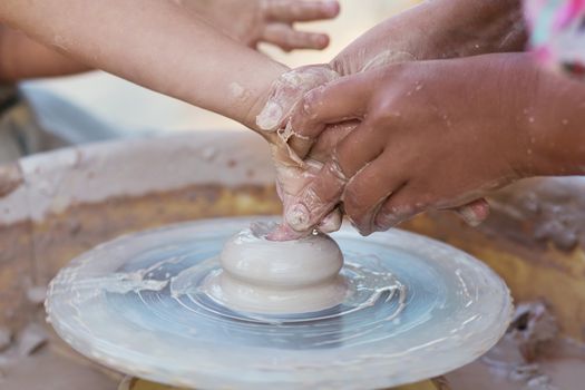 Hands of young potter, creating an earthen jar on the circle, close-up