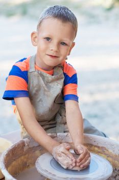 Little smiling boy produced on potters wheel pot. Hands of young potter, creating an earthen jar on the circle, close-up