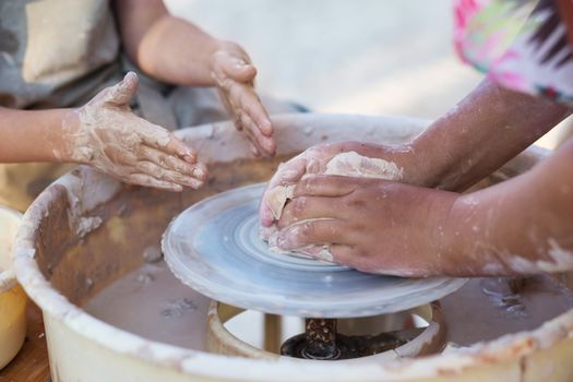 Hands of young potter, creating an earthen jar on the circle, close-up