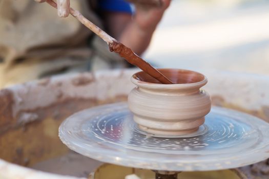 Hands of young potter, creating an earthen jar on the circle, close-up