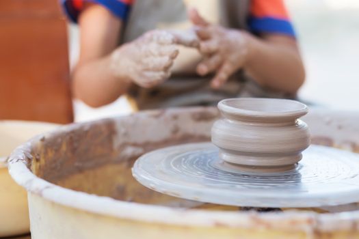 Hands of young potter, creating an earthen jar on the circle, close-up