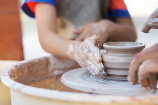 Hands of young potter, creating an earthen jar on the circle, close-up