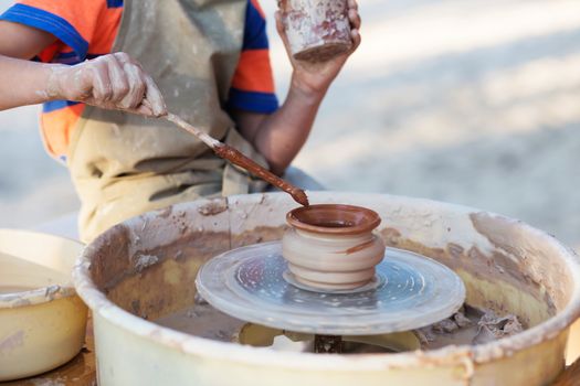 Hands of young potter, creating an earthen jar on the circle, close-up