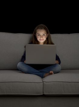 Happy little girl sitting on a couch and working a laptop