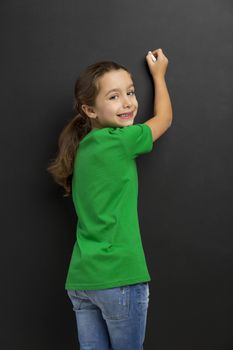 Cute little girl writing in a blackboard, with copy space.