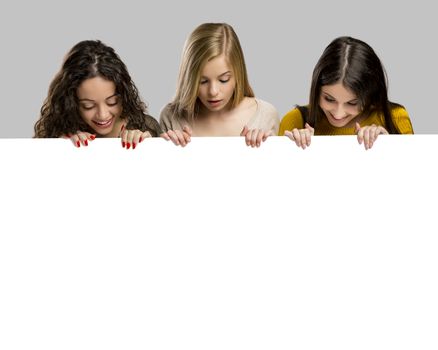 Studio portrait of three girls holding and showing something on a cardboard