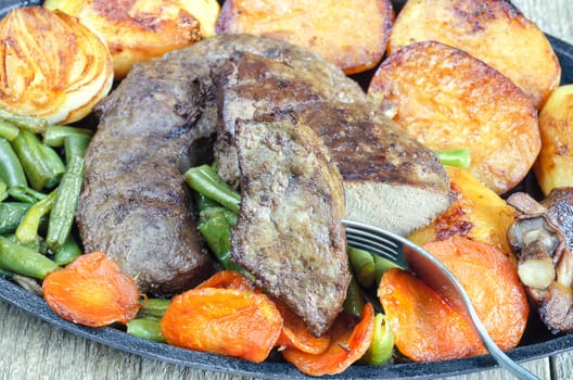 Fried beef liver with vegetables, close-up. Halves of potatoes, onions, whole mushrooms, carrots and green beans