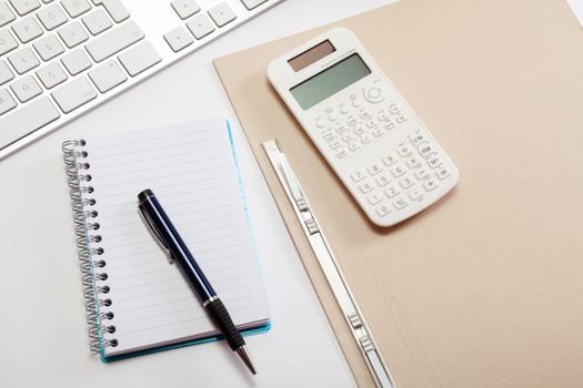 Top view office workplace - keyboard, calculator, pen and notebook on white table