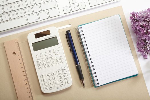 Top view office workplace - keyboard, calculator, pen, flower and notebook on white table