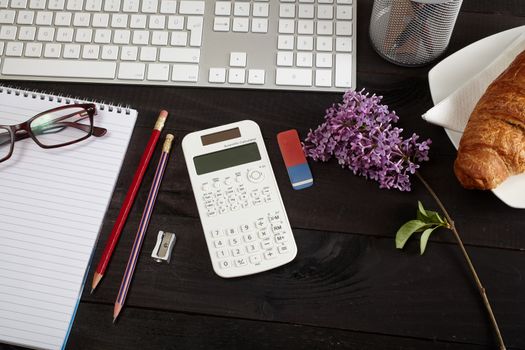 Top view office workplace - keyboard, calculator, pencil, glasses and notebook on black table