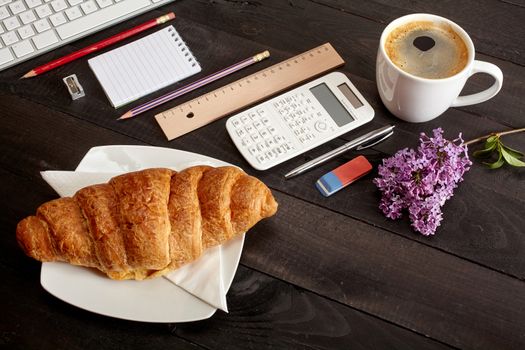 Top view office workplace - coffee, keyboard, pencil, croissant, flower, calculator and notebook on black table
