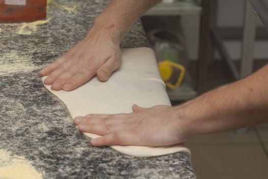 Man chef with raw pizza. Young male in uniform preparing pizza on table.