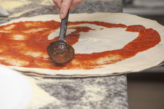 Man chef with raw pizza. Young male in uniform preparing pizza on table.