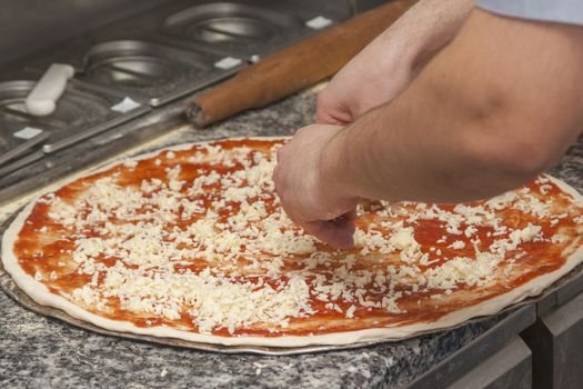 Man chef with raw pizza. Young male in uniform preparing pizza on table.