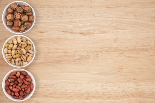 peanuts, hazelnuts, pistachios in a cyan bowl on a wooden table.