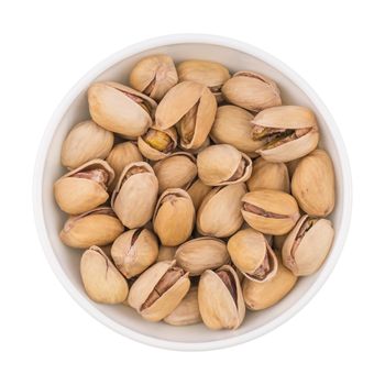 At the center of the frame white bowl with pistachio nuts on a white background. Salted roasted pistachios. Top view.
