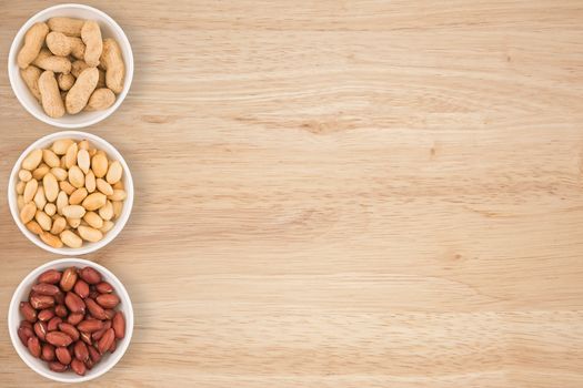 Some peanuts in a cyan bowl on a wooden table.