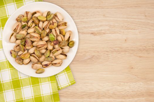 Pistachios in a white plate on a wooden table. top view