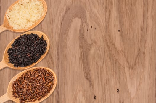 Red, white, and black rice in a wooden spoon on a wooden table