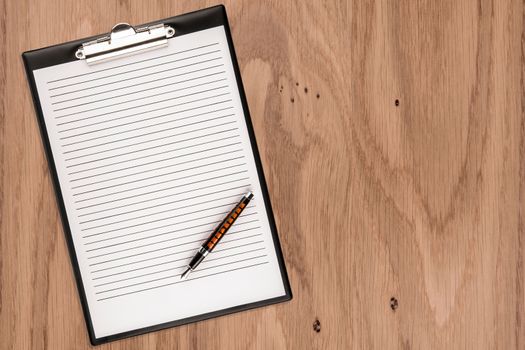 Clipboard with blank paper and pen on wooden desk. Copy space for text