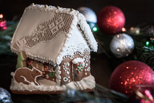 the gingerbread house in the white glaze on the background of the Christmas wreath with Christmas decorations