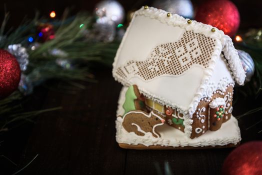 the gingerbread house in the white glaze on the background of the Christmas wreath with Christmas decorations