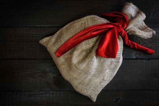 Christmas gift bag with red ribbon on wooden background