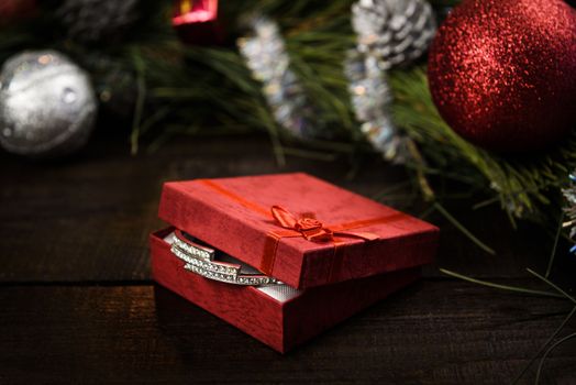 Christmas gift in red box with red ribbon on wooden background, surrounded by a Christmas wreath