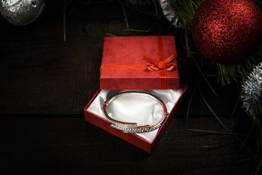 Christmas gift in red box with red ribbon on wooden background, surrounded by a Christmas wreath