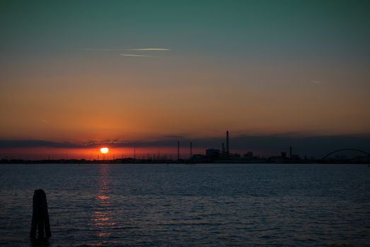 Sea sunset with silhouettes of a chemical industrial hub.