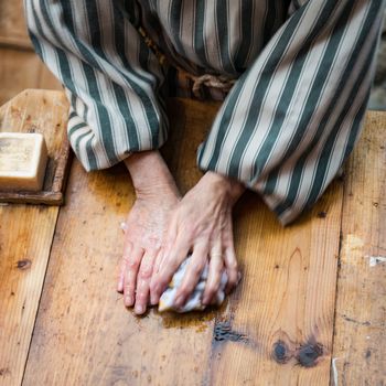 Detail of the hands of a washerwoman washing clothes on a wooden board.