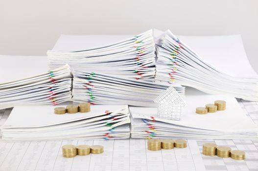 House with step pile of gold coins on pile overload paperwork of report and receipt with colorful paperclip place on finance account with white background.