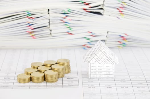 House and step group of gold coins on finance account have blur pile overload paperwork of report and receipt with colorful paperclip as background.