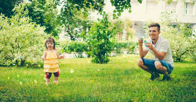Dad and his daughter are making bubbles in the park. Colorful panoram image for modern lifestyle family concept.