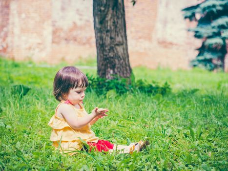 One year old baby girl sitting on grass and looking at his hand. Colorful image with copy space