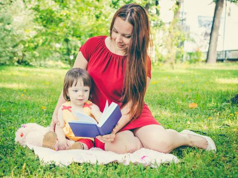 Mother and daughter reading a book outdoors on grass at park