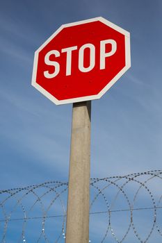 Bright red stop sign against blue sky and razor wire coil