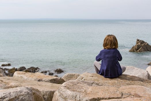 Girl sitting on rock watch watching the ocean waves