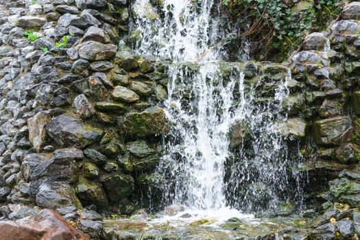 Small waterfall, cascade flowing over mossy boulders in a botanical garden.
