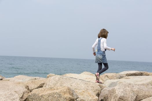 little girl jumping on the rock along the sea