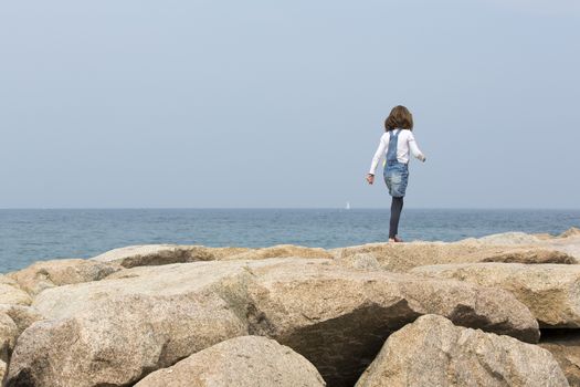 little girl jumping on the rock along the sea