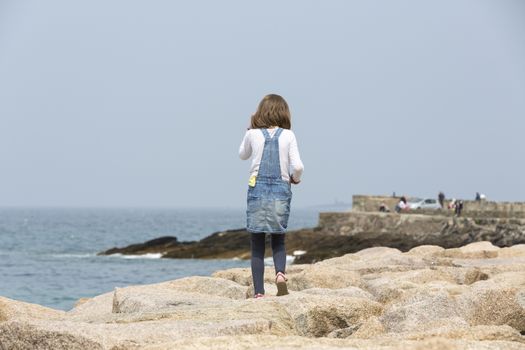 little girl jumping on the rock along the sea