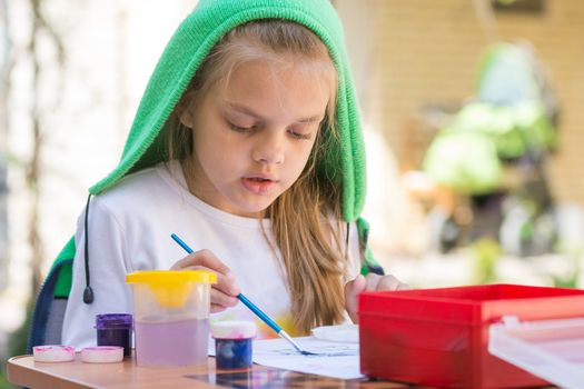 Girl draws paints in the yard in the spring sunny day