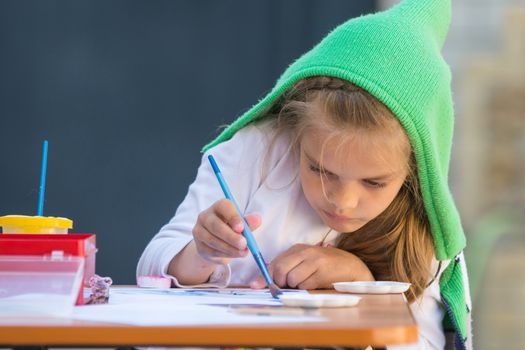 Girl enthusiastically paints watercolors sitting at a table in the yard