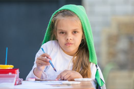 Thoughtful and enthusiastic girl draws a painting at the table and looked at the frame