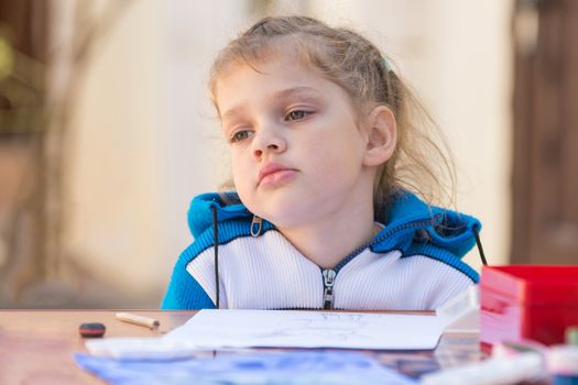 Frustrated girl sitting at a table in the yard and sad looks nowhere