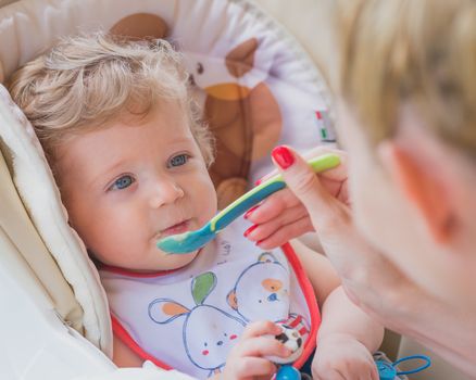 A mother feeding her baby boy with spoon outdoor.