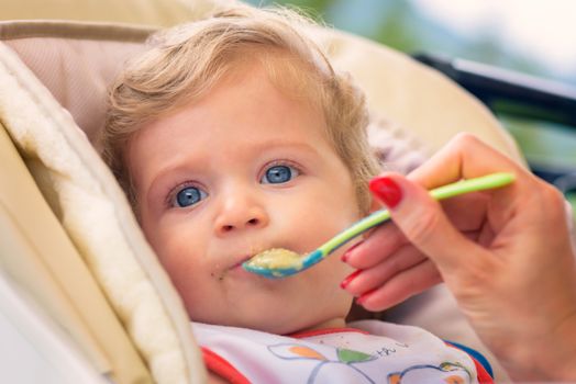 A mother feeding her baby boy with spoon outdoor.